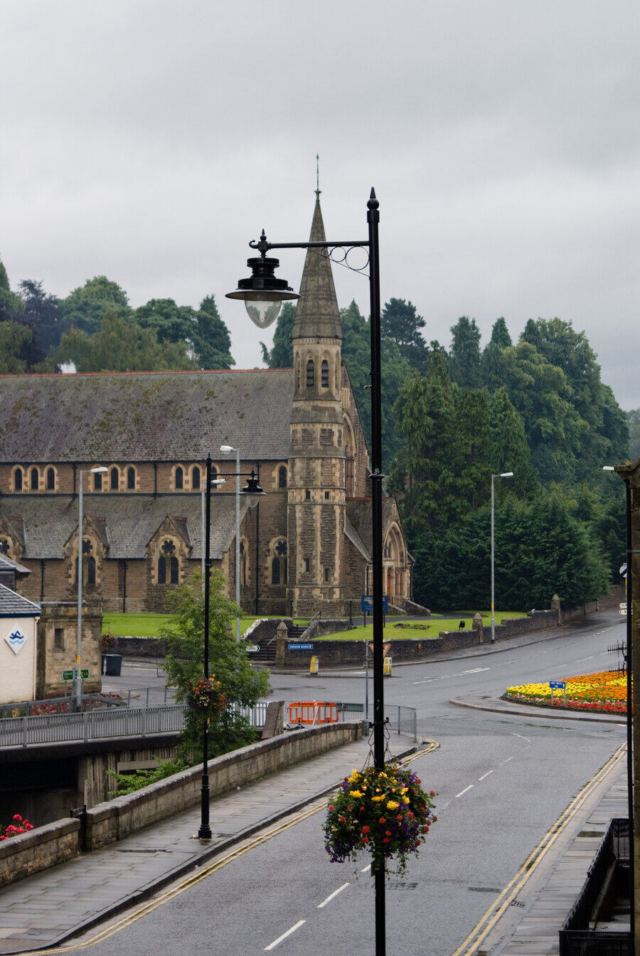 A quiet British town street with a stone church and hanging flower baskets